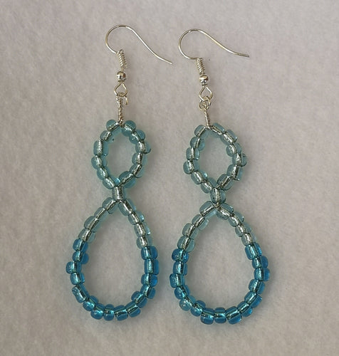 Handmade beaded earrings. silver coloured earring hooks and wire. Beaded part is a figure 8 shape with two shades of blue beads, the darker at the bottom of the 8. Earrings shown laying flat against white felt background