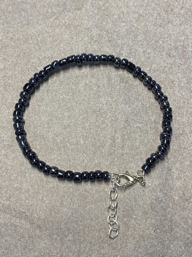 image shows a bracelet against light grey background. bracelet had a single band of dark grey metallic beads and a silver lobster clasp and extender chain