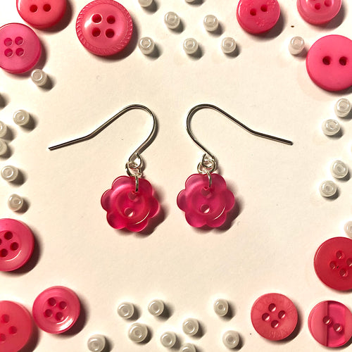 pair of earrings with silver hooks and findings and pink flower buttons. earrings lay flat on white background with border of other pink buttons and small white beads