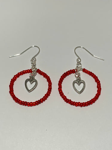 Earrings laying flat against white background. red beads form a circle/hoop around small heart charms. silver coloured charms, findings and earring hooks 