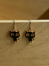 Load image into Gallery viewer, gold coloured earring hooks with black and gold cat charms. Main body of the cat is black with gold eyes, nose, and outline
